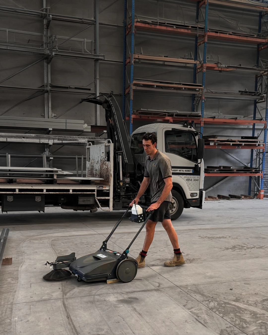 Walk-behind floor cleaning machine operating inside manufacturing facility